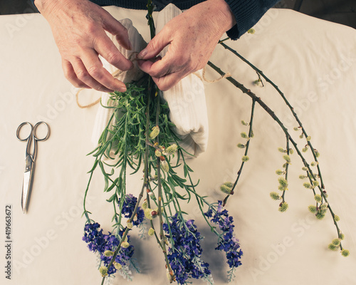 Female hand with purple flowers and willow branches on a white background table surface. photo