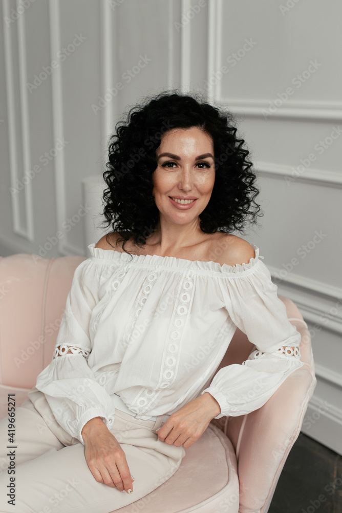 Woman in white blouse with african curls sits on sofa Woman in white blouse with african curls sits on sofa