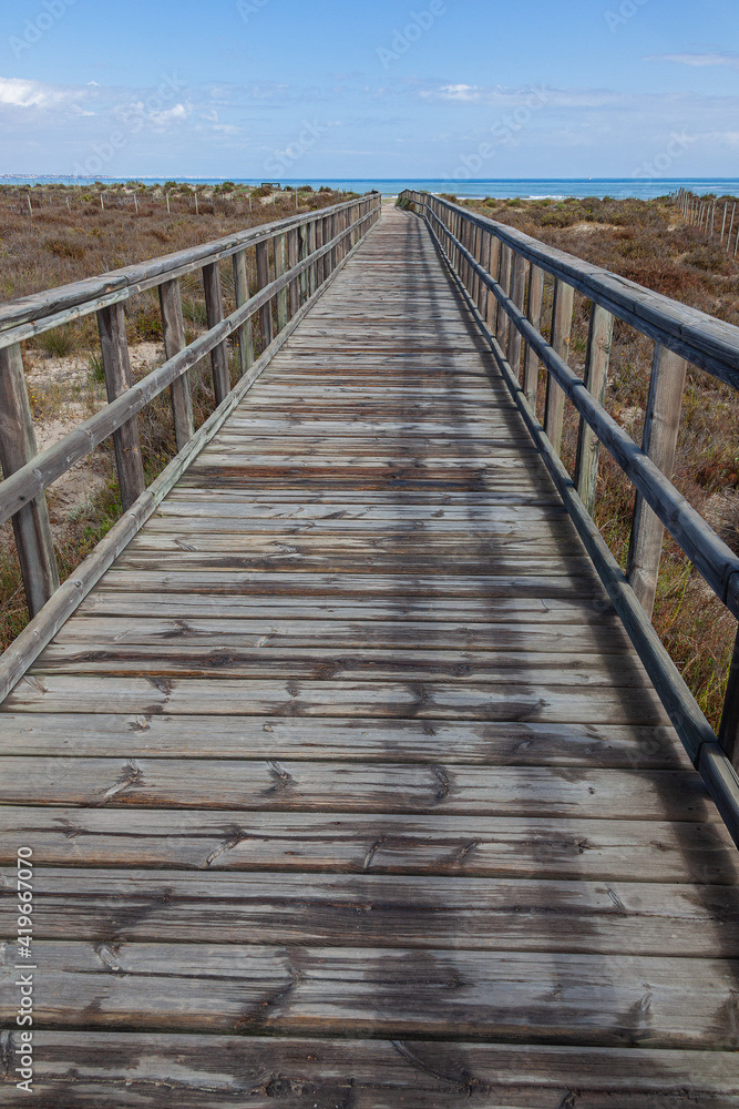 A wooden boardwalk leading through coastal marshlands and sand dunes to the sea beach at San Pedro del Pinatar park, Murcia, Spain