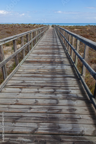 A wooden boardwalk leading through coastal marshlands and sand dunes to the sea beach at San Pedro del Pinatar park, Murcia, Spain