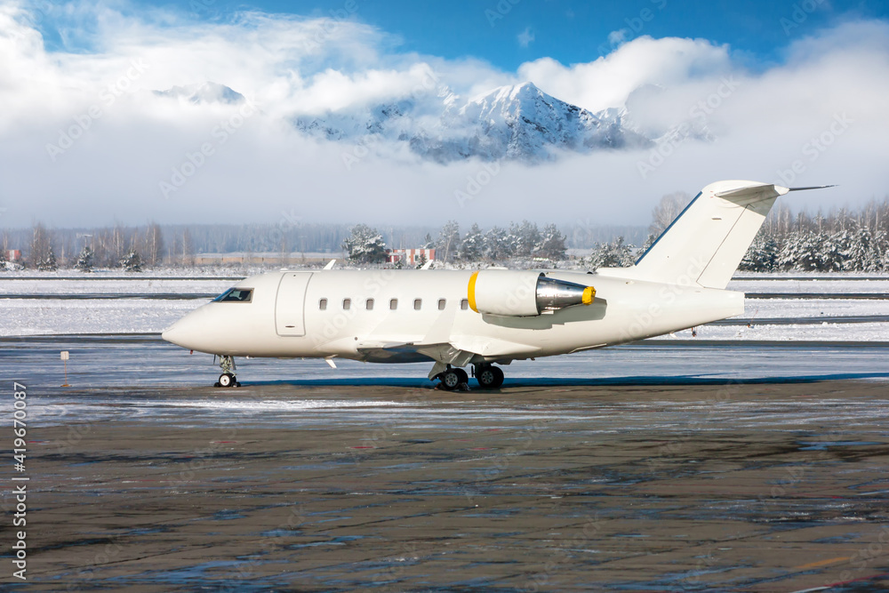 White luxury business jet on the winter airport apron on the background of high scenic mountains on a clear sunny day White luxury business jet on the winter airport apron on the background of high scenic mountains on a clear sunny day