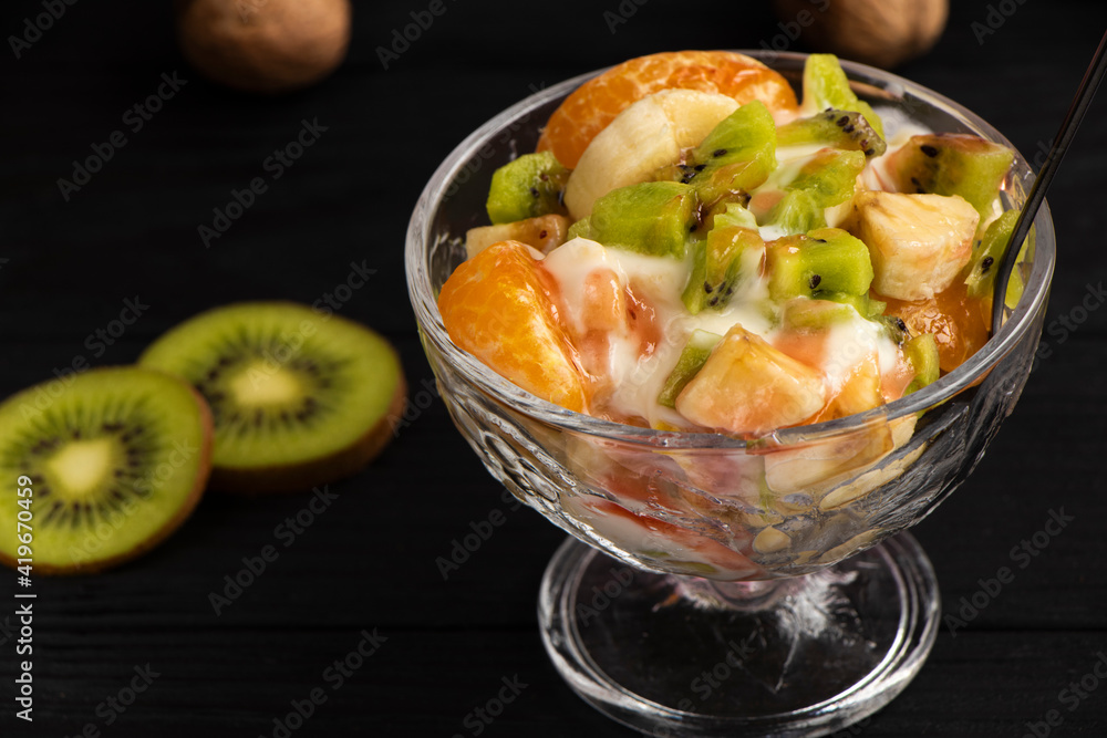 tropical fruit salad in glass bowl. Kiwi, banana and tangerine with yogurt and topping. Veggie dessert. Healthy food concept. Black wood background. High quality photo tropical fruit salad in glass bowl. Kiwi, banana and tangerine with yogurt and topping. Veggie dessert. Healthy food concept. Black wood background. High quality photo