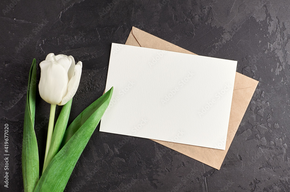 Greeting card with envelope and white tulip flower on black stony background Greeting card with envelope and white tulip flower on black stony background