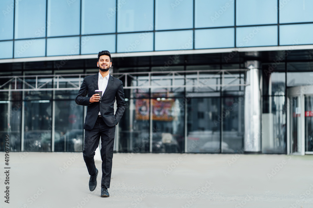 A smiling bearded Indian man walks to an important meeting, behind him a modern building, he smiles and looks at the camera A smiling bearded Indian man walks to an important meeting, behind him a modern building, he smiles and looks at the camera