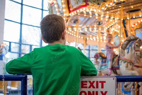 Child looking at merry go round; standing in front of Exit Only sign