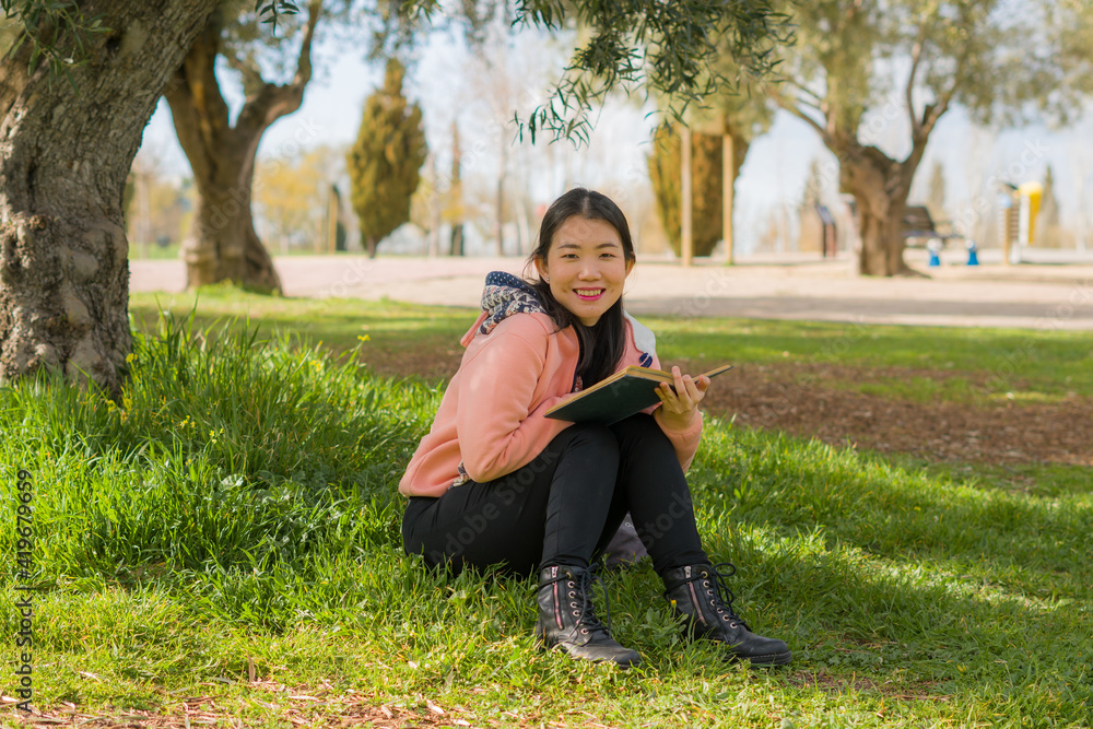 young Asian woman enjoying novel on grass - lifestyle portrait of young happy and pretty Japanese girl reading a book at beautiful city park in reading and studying concept young Asian woman enjoying novel on grass - lifestyle portrait of young happy and pretty Japanese girl reading a book at beautiful city park in reading and studying concept