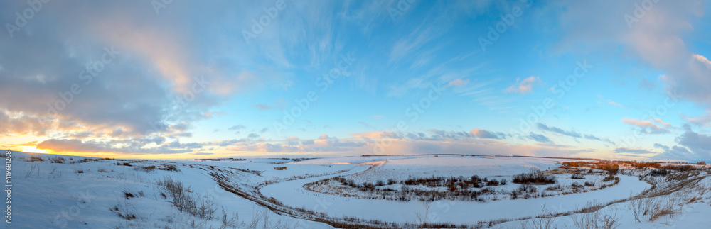 Beautiful panoramic landscape with frozen river and snow covered fields at sunrise.Amazing winter or early springtime scene.