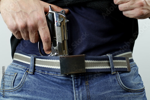 Man is hiding a handgun under the denim belt. Crime concept