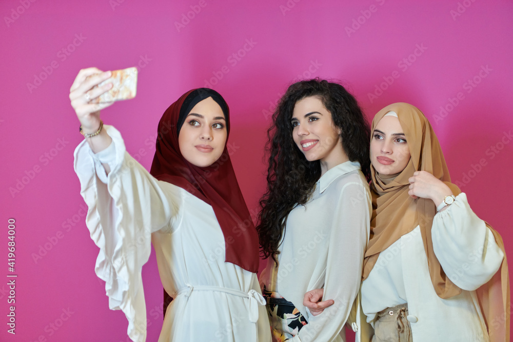 Muslim women taking selfie by mobile phone isolated on pink background Muslim women taking selfie by mobile phone isolated on pink background