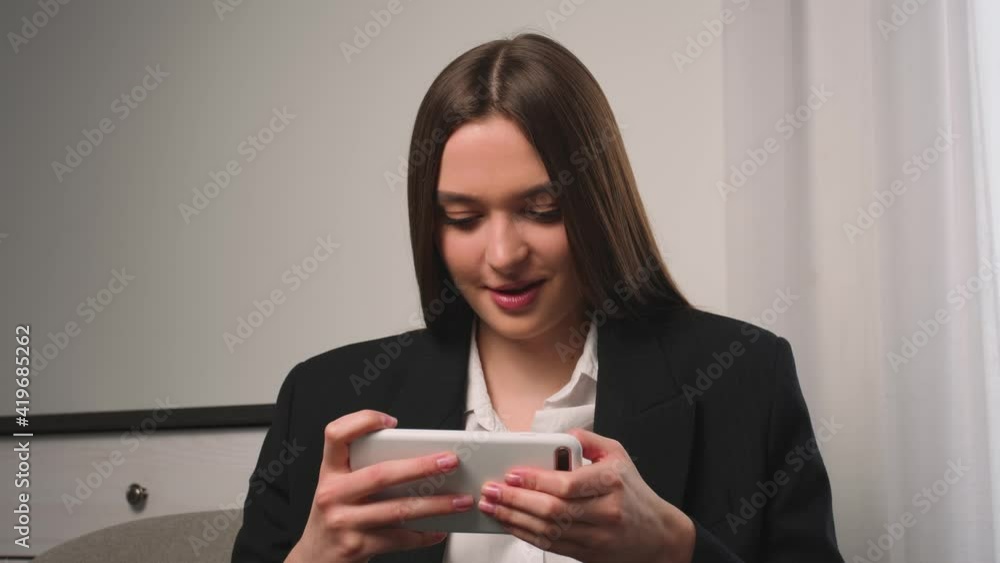 Portrait of young woman plays mobile game on phone at home or office. Attractive woman enjoying smartphone video games. Portrait of young woman plays mobile game on phone at home or office. Attractive woman enjoying smartphone video games.