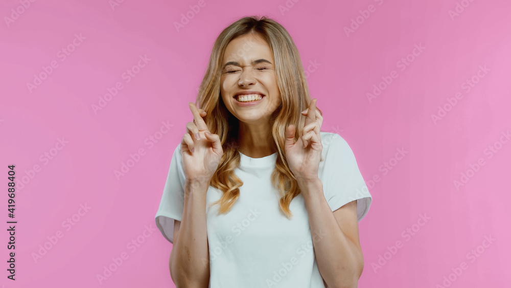 Blonde woman with crossed fingers and closed eyes isolated on pink Blonde woman with crossed fingers and closed eyes isolated on pink