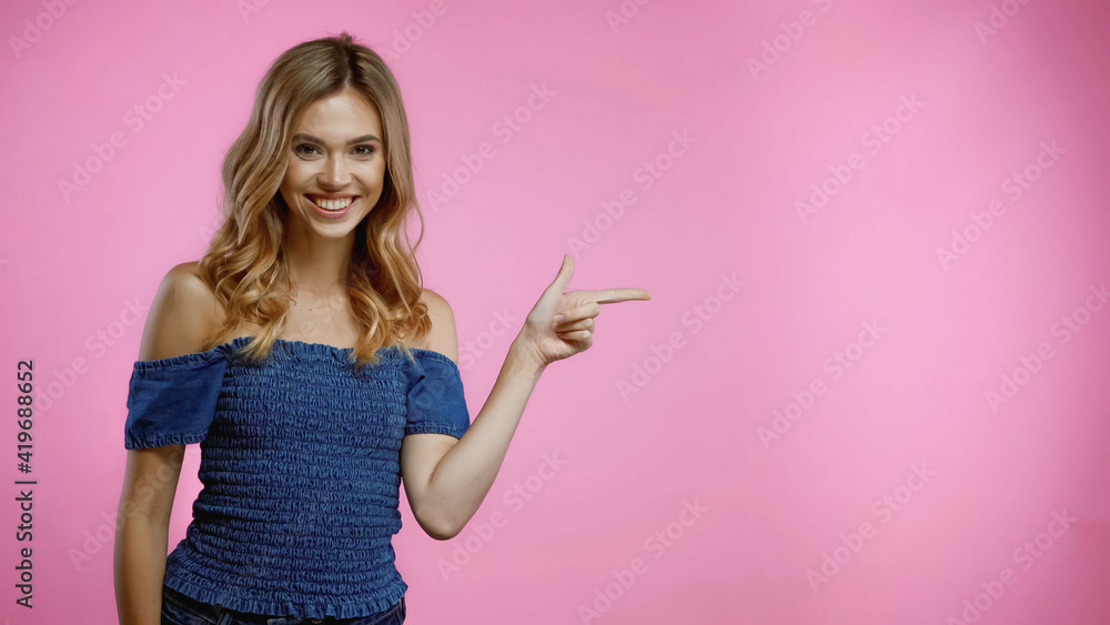 cheerful blonde woman pointing with finger and looking at camera isolated on pink cheerful blonde woman pointing with finger and looking at camera isolated on pink