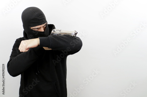 Criminal man wearing balaclava holding pistol, standing shooting with a gun