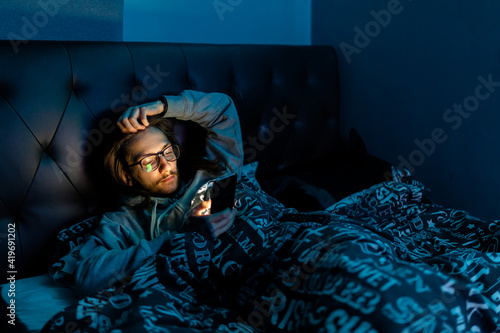 A young man addicted to social media checking his phone before going to bed, Addiction, social media, after dark concept