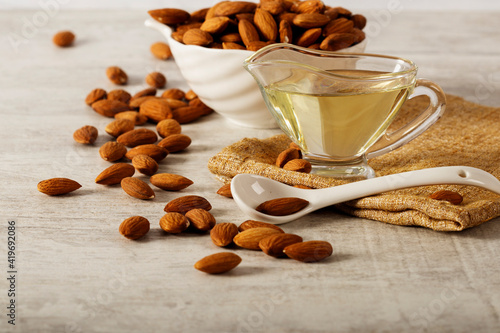 Almond oil with fresh almonds on a white wooden background. Space for text.