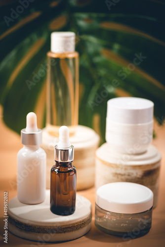 Set of natural cosmetics serum, cream and micellar water with monsterra leaves on pastel blurred background