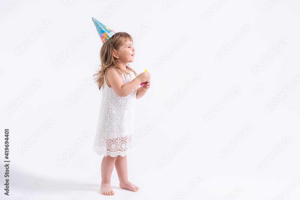 Funny child girl in white dress and birthday hat blowing in whistle on white background Funny child girl in white dress and birthday hat blowing in whistle on white background