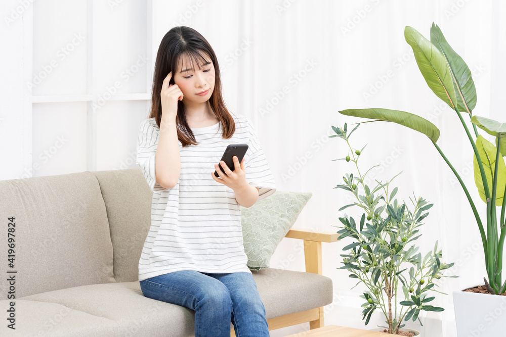 部屋のソファーに座ってスマホを操作する若い女性