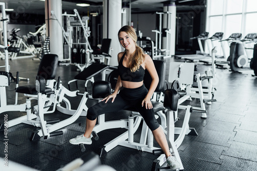 Girl in the gym, a young smiling girl with an athletic body, exercises the exercise on the legs in a modern spacious gym