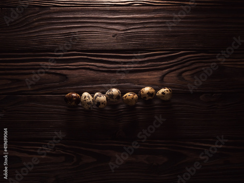 Macrophotography of quail eggs lying in a row. Dark wooden background. Top view