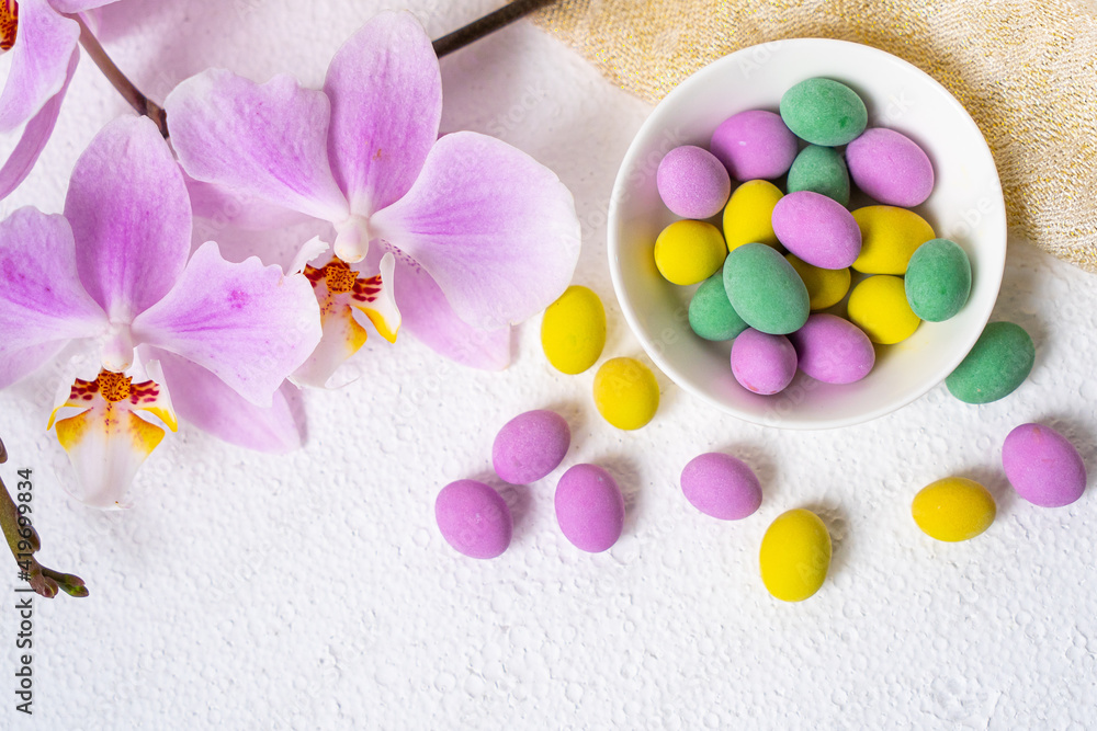 Colorful easter eggs and phalaenopsis orchid flower with plate on white desk. Top view, horisontal. Poster, mock up for design. Selective focus