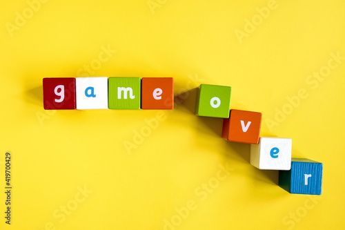Words Game Over made from colored wooden blocks. Painted cubes with letters on yellow background. Top view. Selective focus. Copy space.