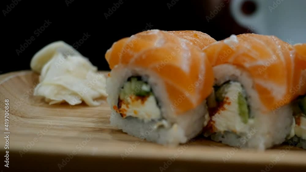 Japanese food. Grab salmon sushi roll with chopsticks from wooden board and lift them up. Selective focus. Close-up. Japanese food. Grab salmon sushi roll with chopsticks from wooden board and lift them up. Selective focus. Close-up.