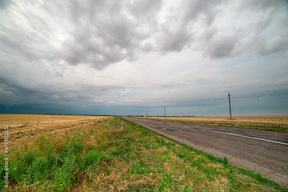 an asphalt road among the fields over which thunderclouds hang