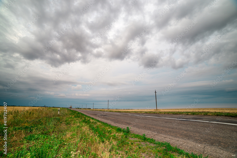 an asphalt road among the fields over which thunderclouds hang an asphalt road among the fields over which thunderclouds hang