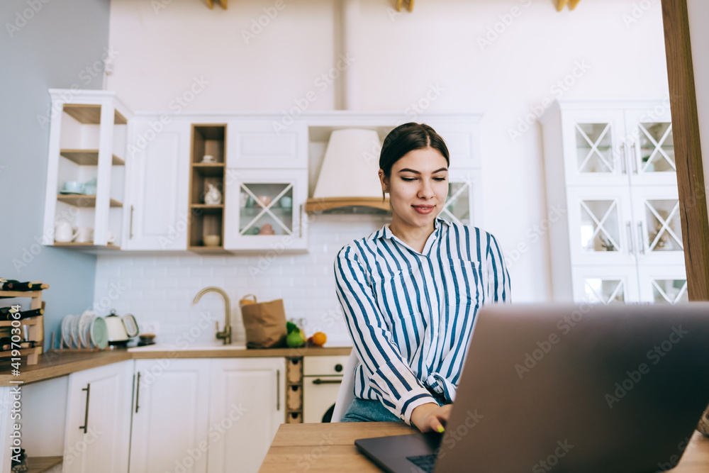 Young caucasian woman using laptop computer, sitting on the kitchen at home. Young caucasian woman using laptop computer, sitting on the kitchen at home.