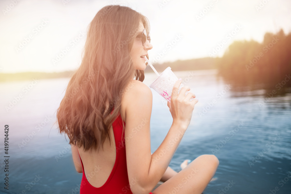 Young woman relax in red swimsuit holds glass with cocktail on beach on glasses, sunlight Young woman relax in red swimsuit holds glass with cocktail on beach on glasses, sunlight
