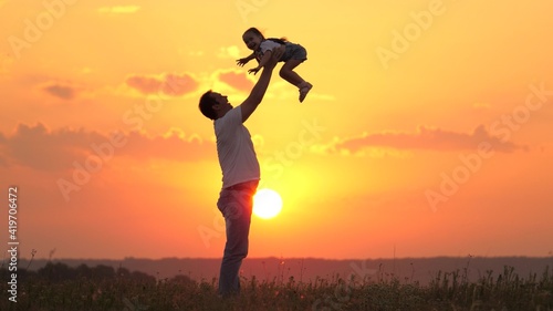 Dad tosses his happy daughter into blue sky at sunset. Father and healthy child play together, laugh and hug. Carefree kid flies into sky. Child is in arms of parent. Dad's day off. Happy family