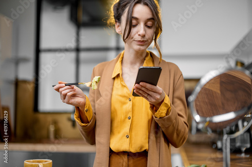 Fussy young businesswoman in a hurry to work in the morning, drinking coffee, chatting on phone and apllying makeup on the go photo