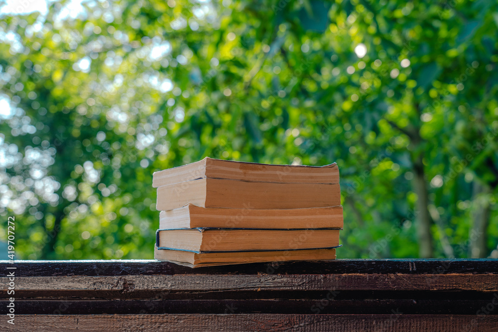 Fototapeta premium Closeup view photography of several vintage paper books laying on organic wooden background isolated on green blurry natural bokeh background