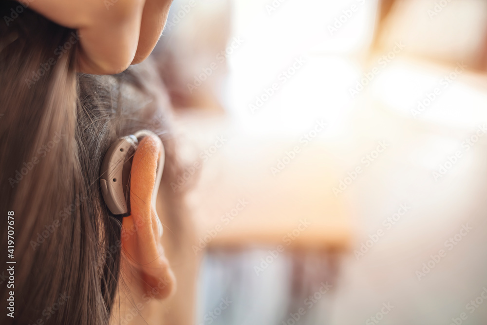 Modern digital in the ear hearing aid for deafness and the hard of hearing patients. Young woman with hearing aid indoors. Young woman with hearing aid on light background. Copy space