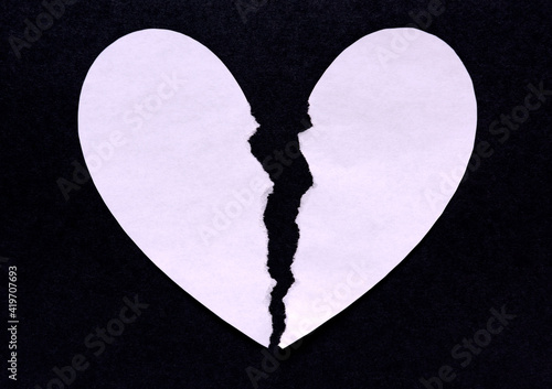 A torn white paper heart on a black background representing a broken heart photo