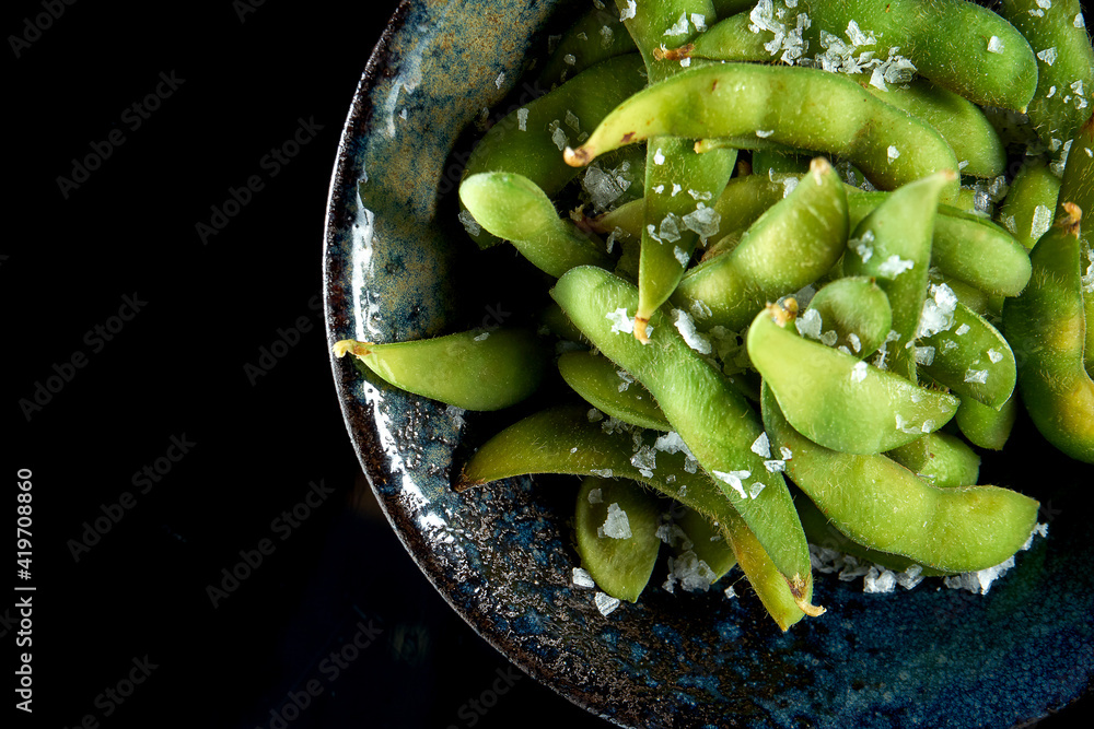 Edamame bean salad with sea salt served in a dark bowl. Isolated on a black background. Restaurant food. Japanese kitchen