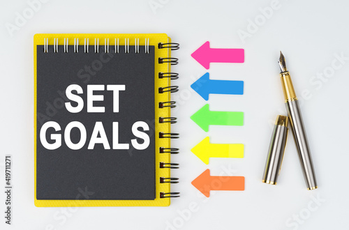 On a white background lies a pen, arrows and a notebook with the inscription - SET GOALS © Dzmitry