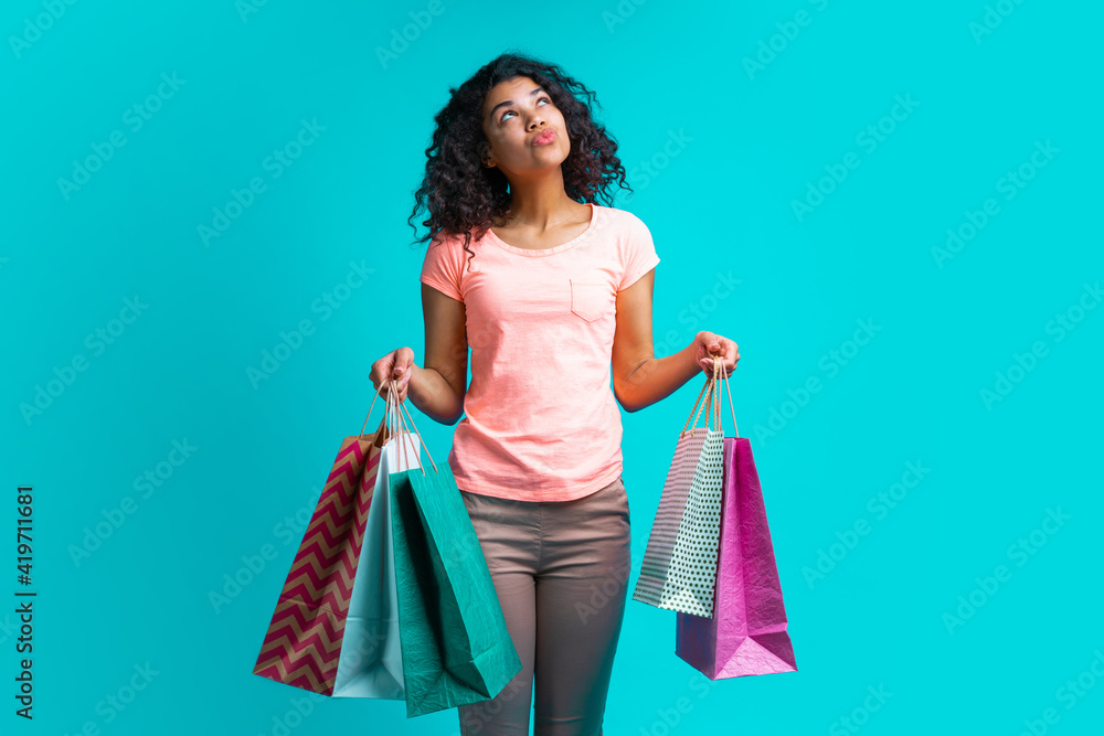 Cute casually dressed african american girl posing with bunches of shopping bags isolated over bright blue background