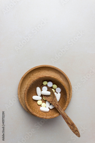A handful of pills in a wooden plate with spoon. The concept of medcine, treatment. Top view. Vertical photo