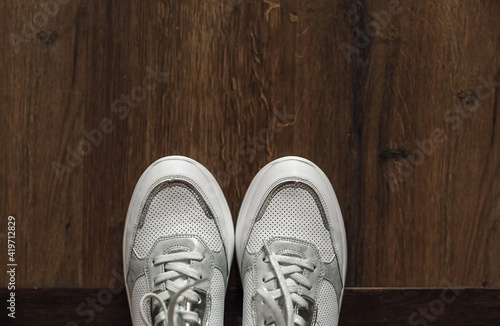 White sneakers on the wooden floor. Top view.