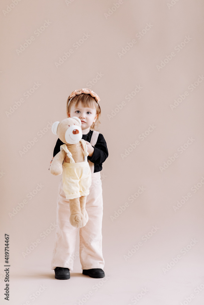 Fototapeta premium My favorite toy. Cute little 2 years old girl hugging her teddy bear and smiling, decorated beige studio background