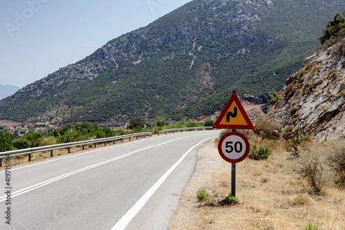 Road sign "steep turn" and "speed limit" on the mountain road (Europe, Greece)