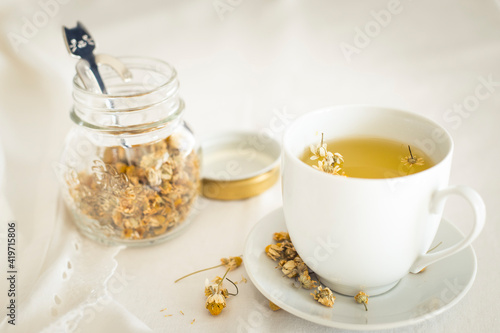 White cup of chamomile tea and glass vase with dried flowers. Foraging idea for natural relaxing infusions. Close up  still life.