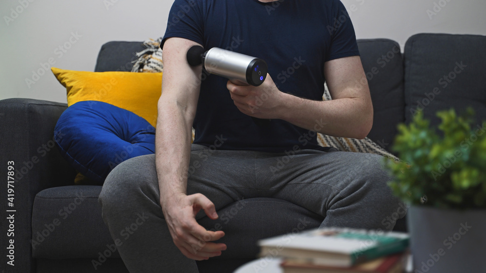 Man massaging arm with massage percussion device at home.