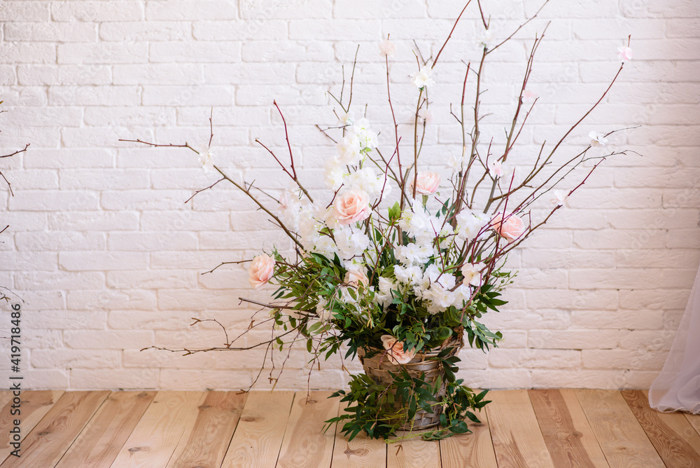 Decorations of branches with beautiful pink and white flowers in the basket against the background of a white brick wall