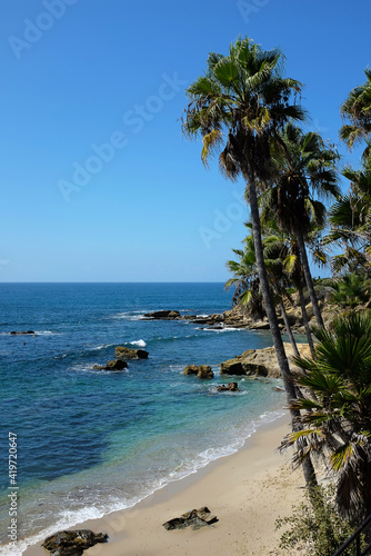 The Laguna Beach Shoreline on a bright blue sky day, seen from a view point in Heisler Park with Palm Trees.