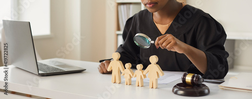 Photos African american judge looking through magnifying glass at wood family figure making decision on children custody