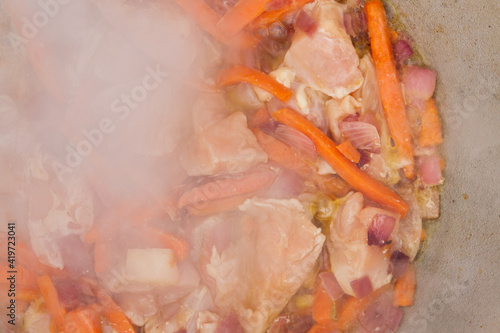 Chicken pieces are fried with carrots and red onions in a cauldron on the grill