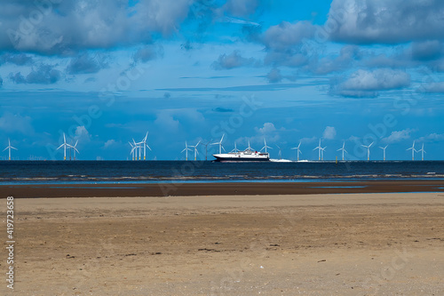 Wind turbines in the sea with a ferry passing and blue sky and sandy beach